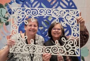 Photo of Eva Dietz and Anne Breight holding a lacy frame in front of them at OnStage in Vancouver Canada in November, 2022.