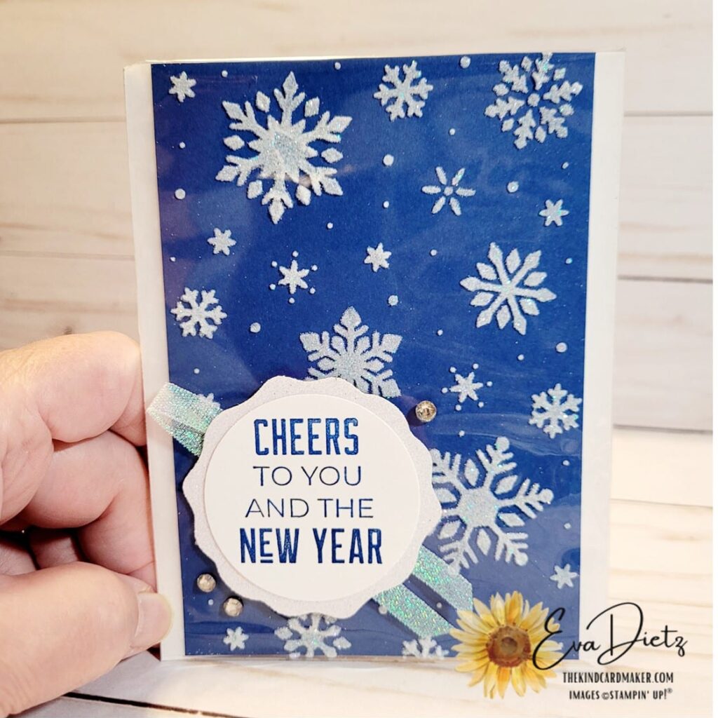 Showing the finished card with the front tag and ribbon on top of the clear envelope enclosing the embossing paste snowflakes design.