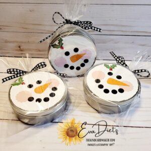 Round Snowman tins filled with mini tootsie rolls and two peppermint patties. Tin has cute paper snowman face. Gift is bagged and tied with a black and white gingham ribbon.