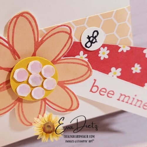 Close Up photo of a Square Pillow Treat Box in white, decorated with a belly band of pink honeycomb pattern, two small flags, one of which says bee mine, and topped off with am 8 petal pink flower with a yellow center covered in white sequins designed by Eva Dietz, The Kind Card Maker.