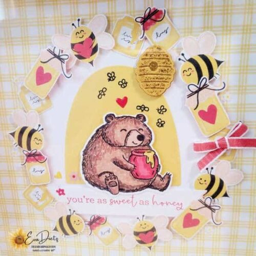 Closeup of a home decor piece that shows a bear with a pot of honey sitting in the middle, surrounded by bumblebees and jars of honey. One red bow finishes it off. Designed by Eva Dietz, The Kind Card Maker.